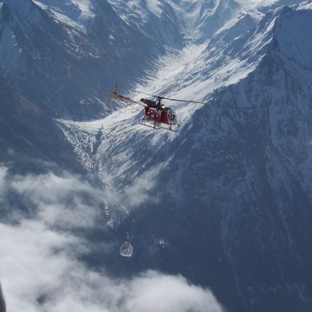 Hélicoptère transportant une charge sous élingue au-dessus d'une vallée alpine